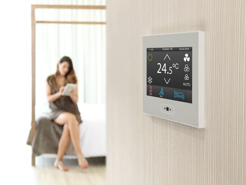 Aparato que mide la temperatura interior de la casa y de fondo una mujer sentada en su cama